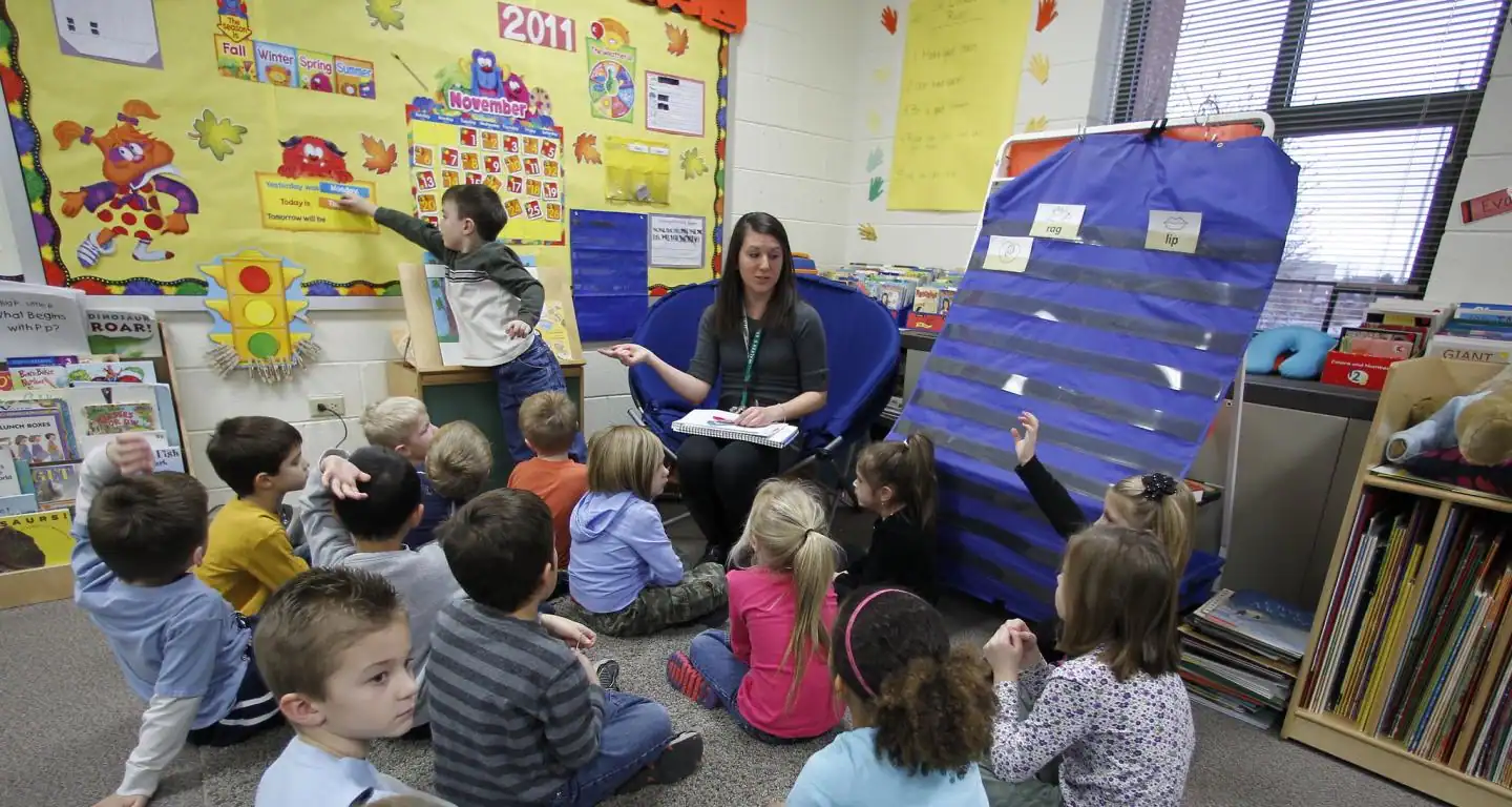 Early-childhood teacher leading circle time with young students during a morning classroom routine, representing lived-experience counselling support for educators