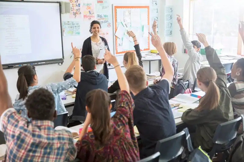 High-school teacher leading an interactive lesson with students raising their hands, highlighting educator engagement and the need for emotional support