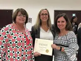 Three teachers celebrating a recognition award symbolizing appreciation and support through the REACH Program by Restored Image Counselling