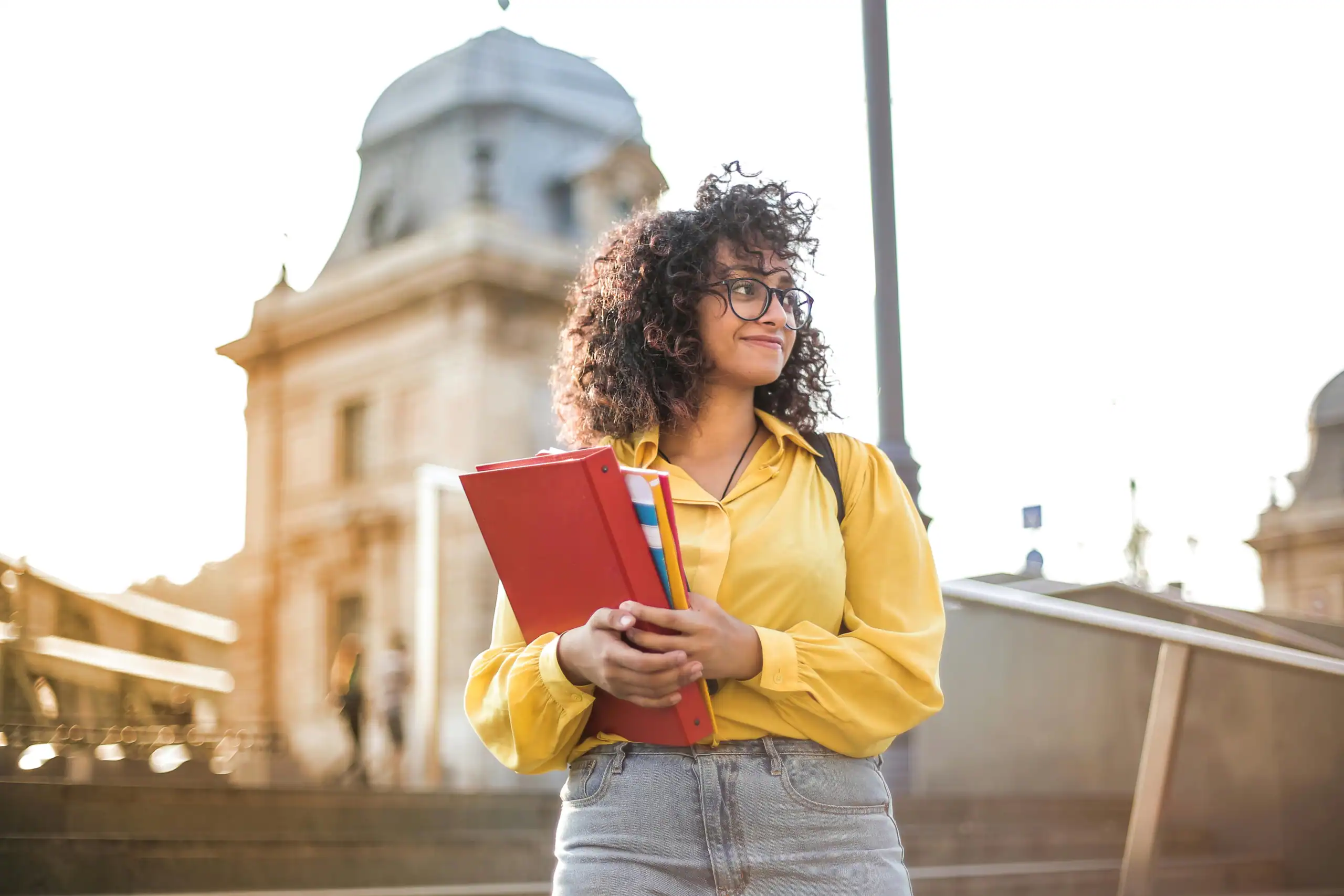 University student holding textbooks and smiling outdoors on campus.