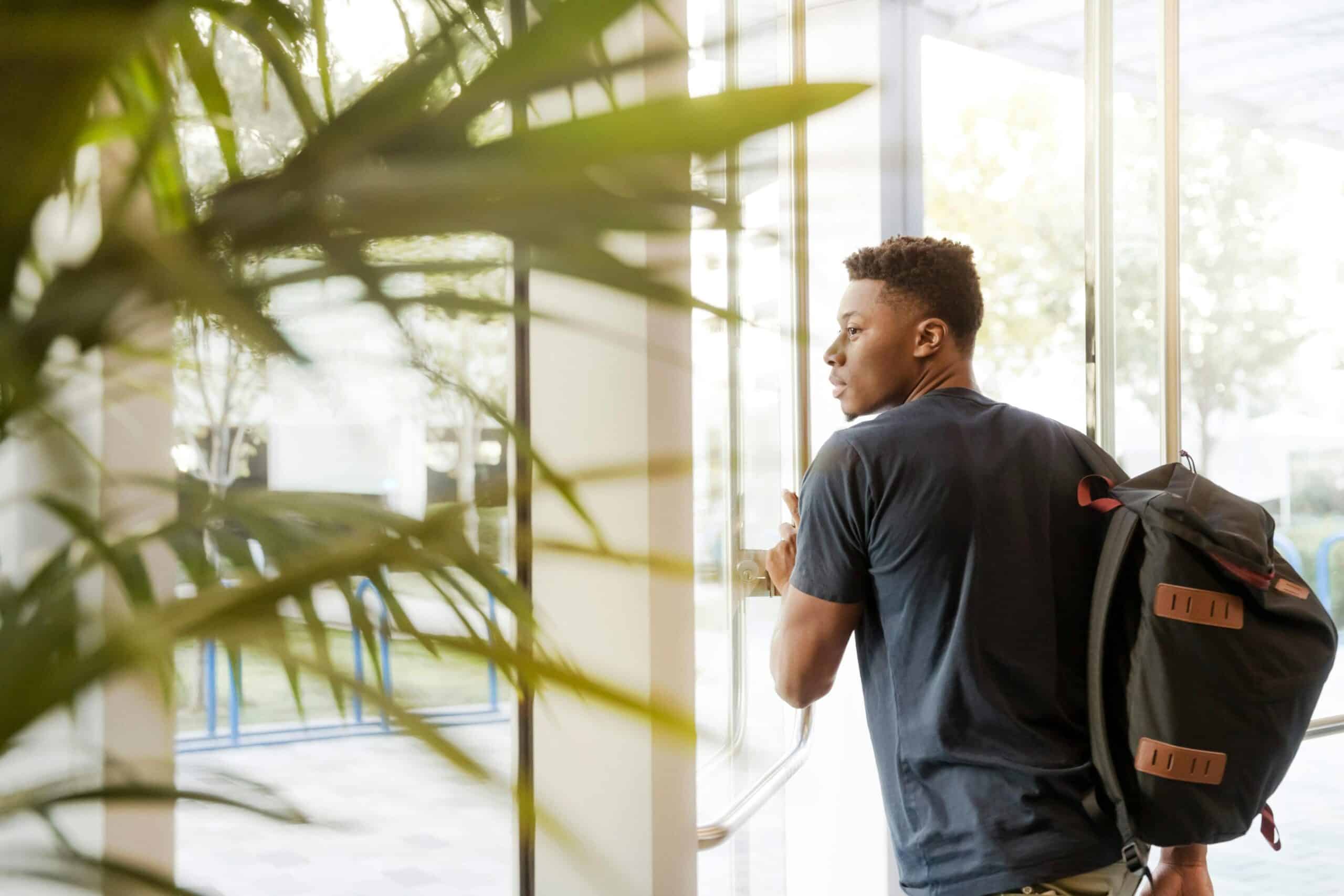 University student entering a campus building with a backpack.