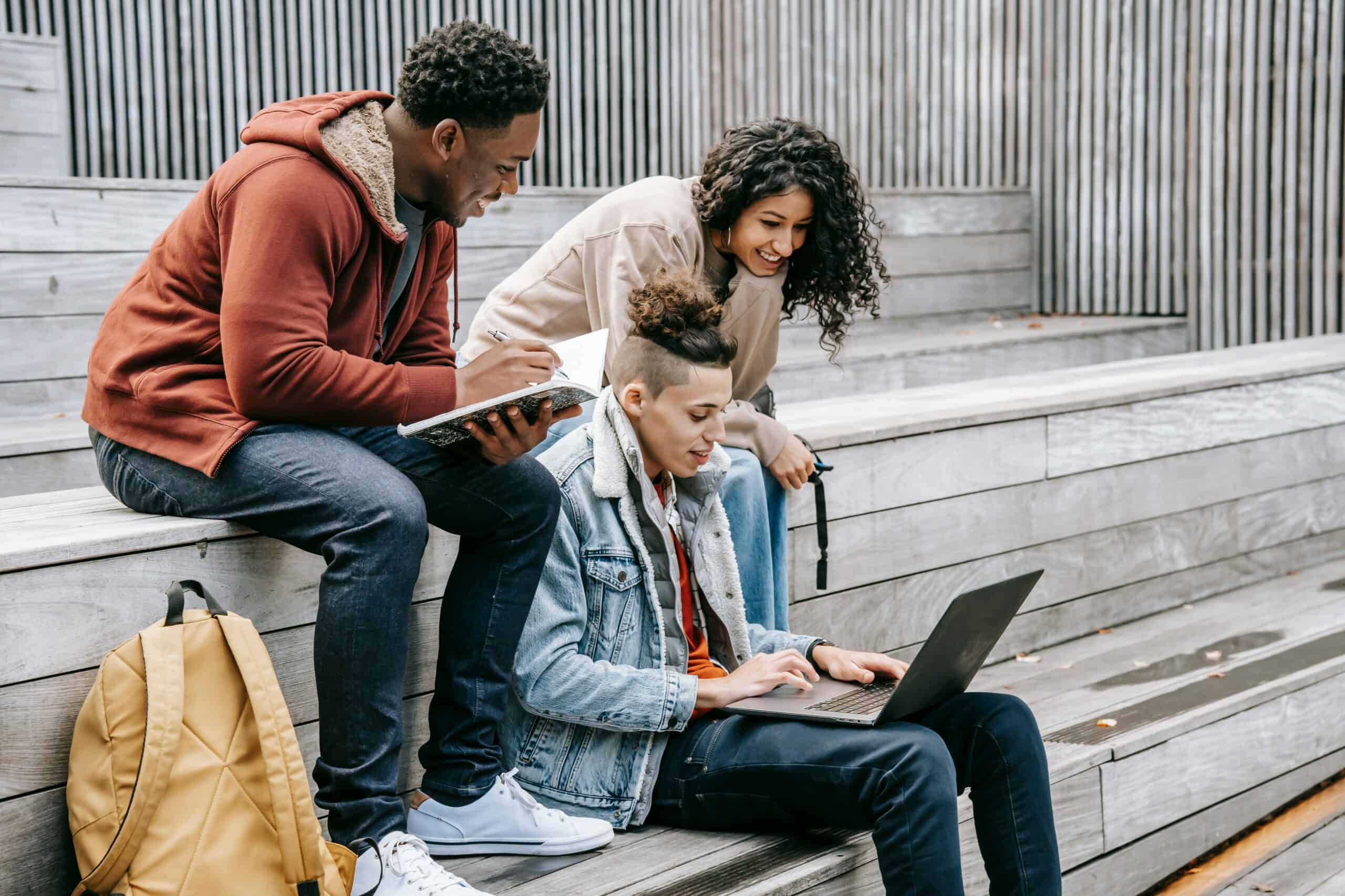 Group of university students studying together outdoors, using a laptop and notebook.