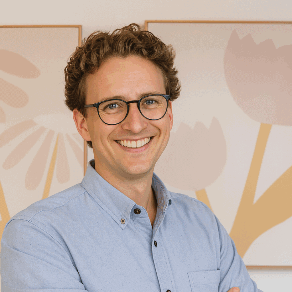 Professional portrait of counsellor Travis Rowe smiling with arms crossed in front of floral artwork.