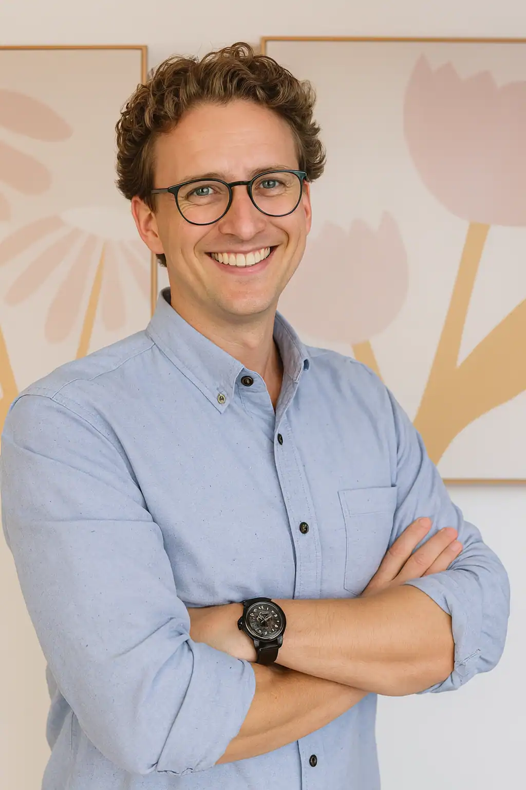 Professional portrait of counsellor Travis Rowe smiling with arms crossed in front of floral artwork.