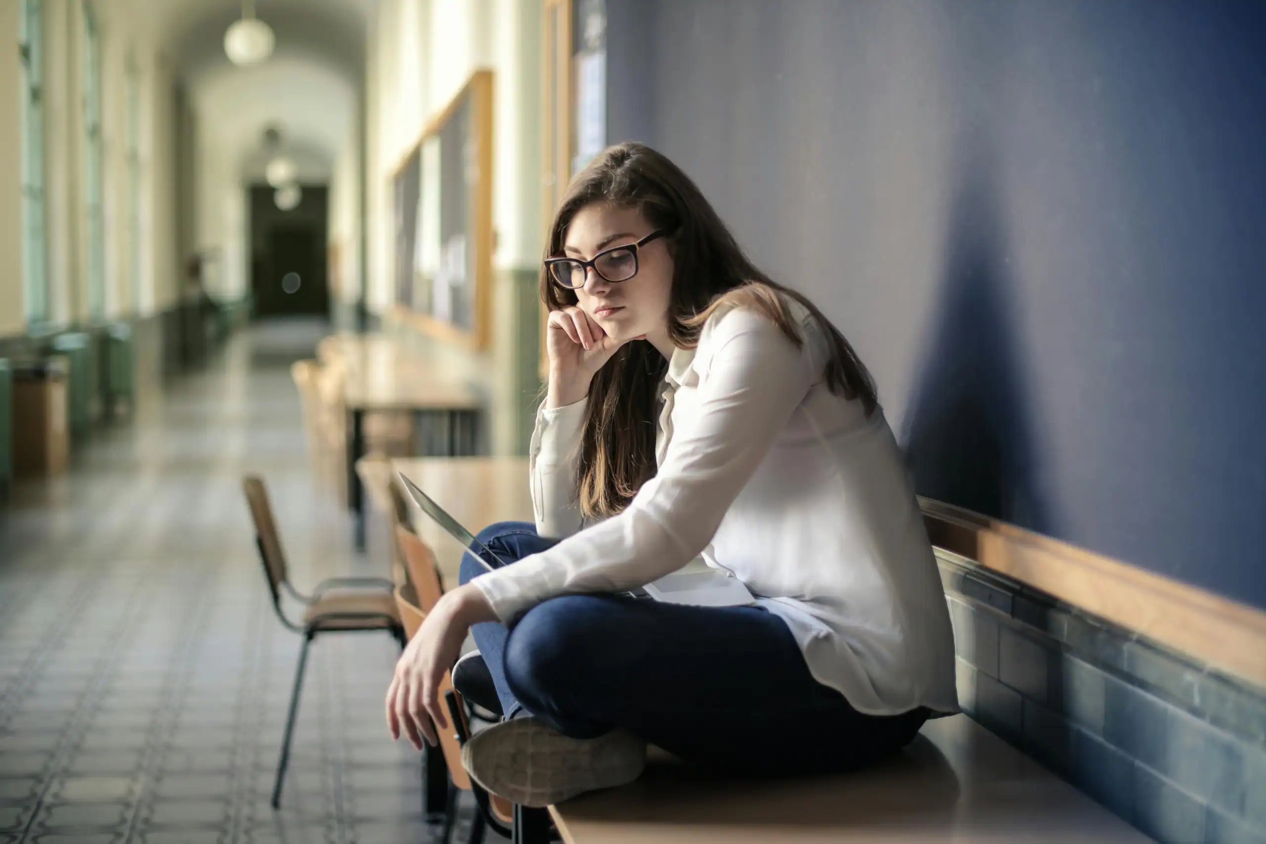 University student sitting alone in a hallway looking overwhelmed with her laptop
